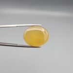 Multi-angle macro photographs of a 19.61-carat natural yellow chalcedony agate (Zard Aqeeq) oval cabochon from Iran held in metal tweezers, highlighting a smooth domed profile, uniform honey-yellow translucency, and a high-gloss reflective surface.