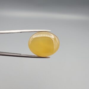 Multi-angle macro photographs of a 19.61-carat natural yellow chalcedony agate (Zard Aqeeq) oval cabochon from Iran held in metal tweezers, highlighting a smooth domed profile, uniform honey-yellow translucency, and a high-gloss reflective surface.
