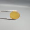 Multi-angle macro photographs of a 19.61-carat natural yellow chalcedony agate (Zard Aqeeq) oval cabochon from Iran held in metal tweezers, highlighting a smooth domed profile, uniform honey-yellow translucency, and a high-gloss reflective surface.
