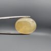 Distinctive 19.78 carat natural yellow chalcedony agate (Zard Aqeeq) from Iran, shaped into a smooth oval cabochon featuring a warm honey-yellow glow and unique natural black inclusions embedded inside.