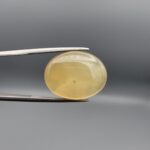 Distinctive 19.78 carat natural yellow chalcedony agate (Zard Aqeeq) from Iran, shaped into a smooth oval cabochon featuring a warm honey-yellow glow and unique natural black inclusions embedded inside.