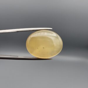 Distinctive 19.78 carat natural yellow chalcedony agate (Zard Aqeeq) from Iran, shaped into a smooth oval cabochon featuring a warm honey-yellow glow and unique natural black inclusions embedded inside.