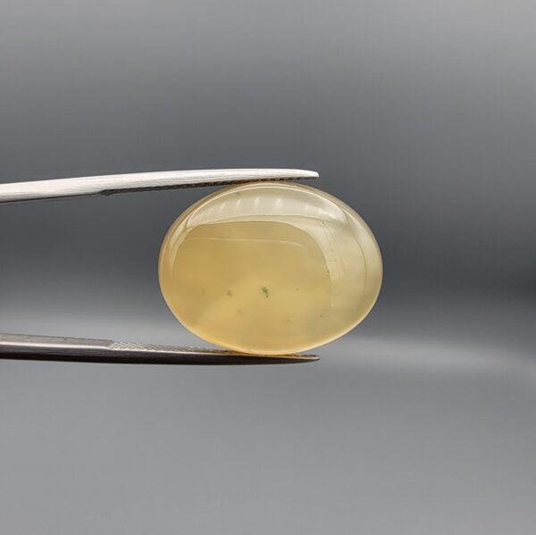 Distinctive 19.78 carat natural yellow chalcedony agate (Zard Aqeeq) from Iran, shaped into a smooth oval cabochon featuring a warm honey-yellow glow and unique natural black inclusions embedded inside.