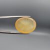 Multi-angle macro photographs of a 19.78-carat natural yellow chalcedony agate (Zard Aqeeq) oval cabochon from Iran held in metal tweezers, showcasing a translucent honey-yellow body with natural internal black inclusions visible on both the front and reverse surfaces.