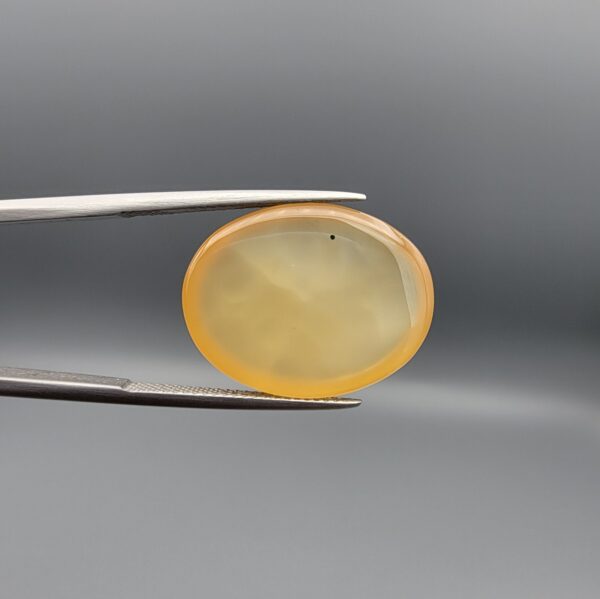 Multi-angle macro photographs of a 19.78-carat natural yellow chalcedony agate (Zard Aqeeq) oval cabochon from Iran held in metal tweezers, showcasing a translucent honey-yellow body with natural internal black inclusions visible on both the front and reverse surfaces.