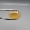 Multi-angle macro photographs of a 16.65-carat natural yellow chalcedony agate (Zard Aqeeq) oval cabochon from Iran held in metal tweezers, highlighting a smooth domed profile, uniform honey-yellow translucency, and a high-gloss reflective surface.
