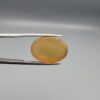 Multi-angle macro photographs of a 16.65-carat natural yellow chalcedony agate (Zard Aqeeq) oval cabochon from Iran held in metal tweezers, highlighting a smooth domed profile, uniform honey-yellow translucency, and a high-gloss reflective surface.