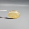 Multi-angle macro photographs of a 25.11-carat natural yellow chalcedony agate (Zard Aqeeq) oval cabochon held in metal tweezers, showcasing a smooth domed profile, uniform honey-yellow translucency, and a high-gloss reflective surface.