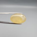 Multi-angle macro photographs of a 25.11-carat natural yellow chalcedony agate (Zard Aqeeq) oval cabochon held in metal tweezers, showcasing a smooth domed profile, uniform honey-yellow translucency, and a high-gloss reflective surface.