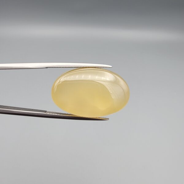 Multi-angle macro photographs of a 25.11-carat natural yellow chalcedony agate (Zard Aqeeq) oval cabochon held in metal tweezers, showcasing a smooth domed profile, uniform honey-yellow translucency, and a high-gloss reflective surface.