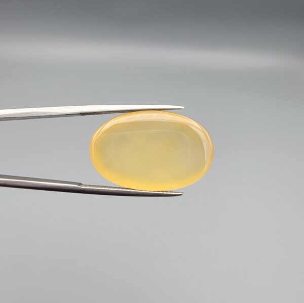 Multi-angle macro photographs of a 25.11-carat natural yellow chalcedony agate (Zard Aqeeq) oval cabochon held in metal tweezers, showcasing a smooth domed profile, uniform honey-yellow translucency, and a high-gloss reflective surface.