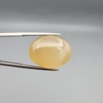 Multi-angle macro photographs of a 27.91-carat natural yellow chalcedony agate (Zard Aqeeq) oval cabochon from Iran held in metal tweezers, showcasing a smooth, domed profile, uniform honey-yellow translucency, and a high-gloss reflective surface.