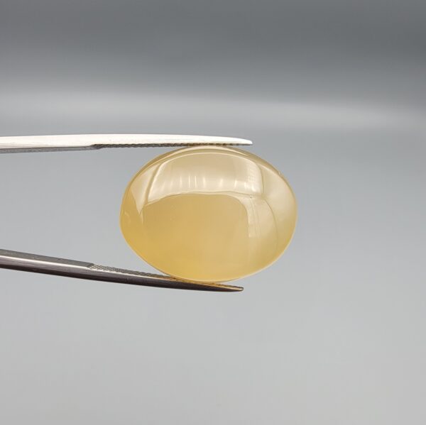Multi-angle macro photographs of a 27.91-carat natural yellow chalcedony agate (Zard Aqeeq) oval cabochon from Iran held in metal tweezers, showcasing a smooth, domed profile, uniform honey-yellow translucency, and a high-gloss reflective surface.