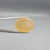 Multi-angle macro photographs of a 27.91-carat natural yellow chalcedony agate (Zard Aqeeq) oval cabochon from Iran held in metal tweezers, showcasing a smooth, domed profile, uniform honey-yellow translucency, and a high-gloss reflective surface.