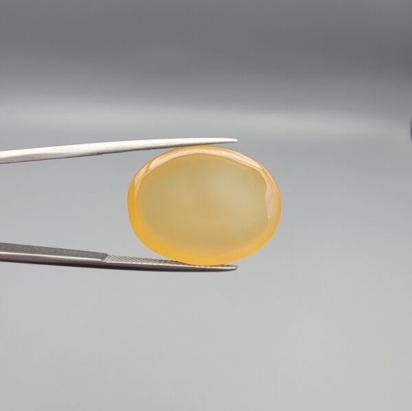 Multi-angle macro photographs of a 27.91-carat natural yellow chalcedony agate (Zard Aqeeq) oval cabochon from Iran held in metal tweezers, showcasing a smooth, domed profile, uniform honey-yellow translucency, and a high-gloss reflective surface.