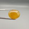 Multi-angle macro photographs of a 19.79-carat natural yellow chalcedony agate (Zard Aqeeq) oval cabochon from Iran held in metal tweezers, showcasing a smooth, domed surface, uniform honey-yellow translucency, and a high-gloss finish.