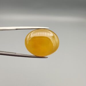 Multi-angle macro photographs of a 19.79-carat natural yellow chalcedony agate (Zard Aqeeq) oval cabochon from Iran held in metal tweezers, showcasing a smooth, domed surface, uniform honey-yellow translucency, and a high-gloss finish.