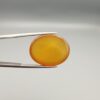 Multi-angle macro photographs of a 19.79-carat natural yellow chalcedony agate (Zard Aqeeq) oval cabochon from Iran held in metal tweezers, showcasing a smooth, domed surface, uniform honey-yellow translucency, and a high-gloss finish.