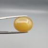 Multi-angle macro photographs of a 15.98-carat natural warm honey yellow chalcedony agate (Shehedi Zard Aqeeq) oval cabochon from Iran held in metal tweezers, showcasing a smooth domed profile, rich honey-colored translucency, and a mirror-like finish.