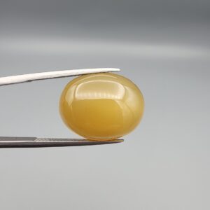 Multi-angle macro photographs of a 15.98-carat natural warm honey yellow chalcedony agate (Shehedi Zard Aqeeq) oval cabochon from Iran held in metal tweezers, showcasing a smooth domed profile, rich honey-colored translucency, and a mirror-like finish.
