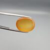 Multi-angle macro photographs of a 15.98-carat natural warm honey yellow chalcedony agate (Shehedi Zard Aqeeq) oval cabochon from Iran held in metal tweezers, showcasing a smooth domed profile, rich honey-colored translucency, and a mirror-like finish.