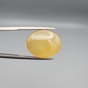Multi-angle macro photographs of a 19.69-carat natural yellow chalcedony agate (Zard Aqeeq) oval cabochon from Iran held in metal tweezers, showcasing a smooth, domed surface, uniform honey-yellow translucency, and a high-gloss finish.