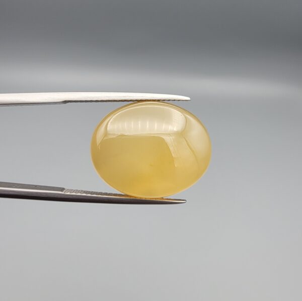 Multi-angle macro photographs of a 19.69-carat natural yellow chalcedony agate (Zard Aqeeq) oval cabochon from Iran held in metal tweezers, showcasing a smooth, domed surface, uniform honey-yellow translucency, and a high-gloss finish.