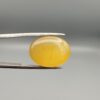 Multi-angle macro photographs of a 15.57-carat natural yellow chalcedony agate (Zard Aqeeq) oval cabochon from Iran held in metal tweezers, showcasing a smooth, domed surface, uniform honey-yellow translucency, and distinct natural internal vein inclusions.