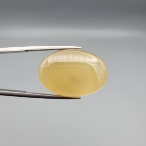 Multi-angle macro photographs of a 27.49-carat natural yellow chalcedony agate (Zard Aqeeq) oval cabochon from Iran held in metal tweezers, showcasing a smooth, domed profile, uniform honey-yellow translucency, and a high-gloss reflective surface.