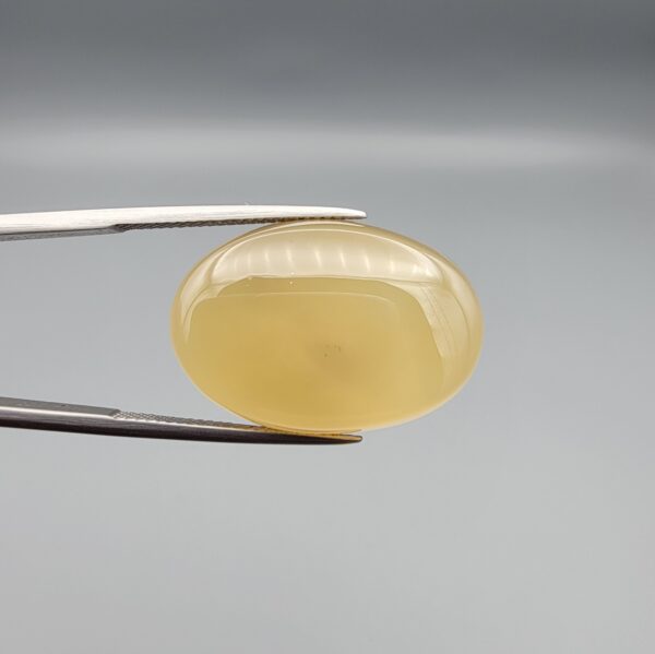 Multi-angle macro photographs of a 27.49-carat natural yellow chalcedony agate (Zard Aqeeq) oval cabochon from Iran held in metal tweezers, showcasing a smooth, domed profile, uniform honey-yellow translucency, and a high-gloss reflective surface.