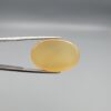 Multi-angle macro photographs of a 27.49-carat natural yellow chalcedony agate (Zard Aqeeq) oval cabochon from Iran held in metal tweezers, showcasing a smooth, domed profile, uniform honey-yellow translucency, and a high-gloss reflective surface.