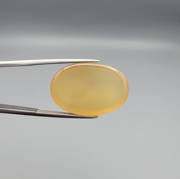 Multi-angle macro photographs of a 27.49-carat natural yellow chalcedony agate (Zard Aqeeq) oval cabochon from Iran held in metal tweezers, showcasing a smooth, domed profile, uniform honey-yellow translucency, and a high-gloss reflective surface.