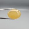 Multi-angle macro photographs of a 32.04-carat natural yellow chalcedony agate (Zard Aqeeq) oval cabochon from Iran held in metal tweezers, showcasing a smooth, domed profile, uniform honey-yellow translucency, and a high-gloss reflective surface.