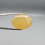 Multi-angle macro photographs of a 32.04-carat natural yellow chalcedony agate (Zard Aqeeq) oval cabochon from Iran held in metal tweezers, showcasing a smooth, domed profile, uniform honey-yellow translucency, and a high-gloss reflective surface.