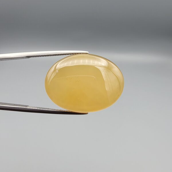 Multi-angle macro photographs of a 32.04-carat natural yellow chalcedony agate (Zard Aqeeq) oval cabochon from Iran held in metal tweezers, showcasing a smooth, domed profile, uniform honey-yellow translucency, and a high-gloss reflective surface.