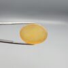 Multi-angle macro photographs of a 32.04-carat natural yellow chalcedony agate (Zard Aqeeq) oval cabochon from Iran held in metal tweezers, showcasing a smooth, domed profile, uniform honey-yellow translucency, and a high-gloss reflective surface.
