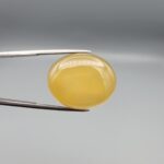 Multi-angle macro photographs of a 35.41-carat natural yellow chalcedony agate (Zard Aqeeq) oval cabochon from Iran held in metal tweezers, showcasing a smooth, domed profile, uniform honey-yellow translucency, and a high-gloss reflective surface.