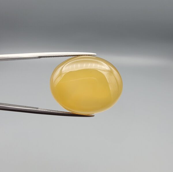 Multi-angle macro photographs of a 35.41-carat natural yellow chalcedony agate (Zard Aqeeq) oval cabochon from Iran held in metal tweezers, showcasing a smooth, domed profile, uniform honey-yellow translucency, and a high-gloss reflective surface.
