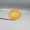 Multi-angle macro photographs of a 35.41-carat natural yellow chalcedony agate (Zard Aqeeq) oval cabochon from Iran held in metal tweezers, showcasing a smooth, domed profile, uniform honey-yellow translucency, and a high-gloss reflective surface.