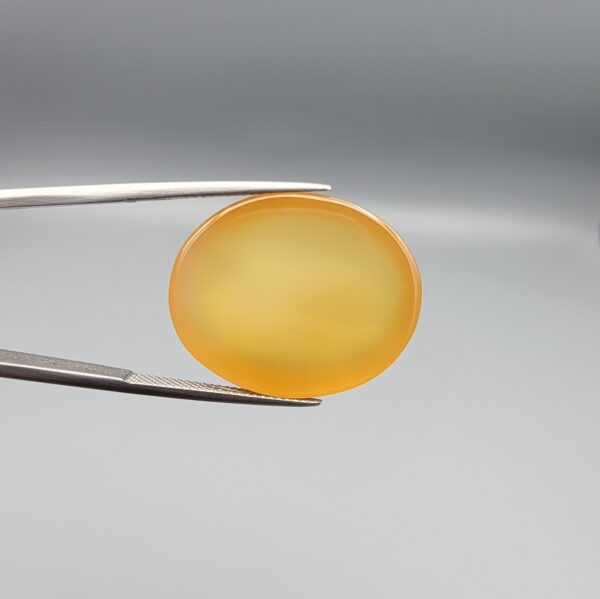Multi-angle macro photographs of a 35.41-carat natural yellow chalcedony agate (Zard Aqeeq) oval cabochon from Iran held in metal tweezers, showcasing a smooth, domed profile, uniform honey-yellow translucency, and a high-gloss reflective surface.