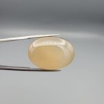 Multi-angle macro photographs of a 41.75-carat natural yellow chalcedony agate (Zard Aqeeq) oval cabochon from Iran held in metal tweezers, showcasing a smooth, domed profile, uniform honey-yellow translucency, and a high-gloss reflective surface.