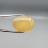 Multi-angle macro photographs of a 31.35-carat natural yellow chalcedony agate (Zard Aqeeq) oval cabochon from Iran held in metal tweezers, showcasing a smooth, domed profile, uniform honey-yellow translucency, and a high-gloss reflective surface.