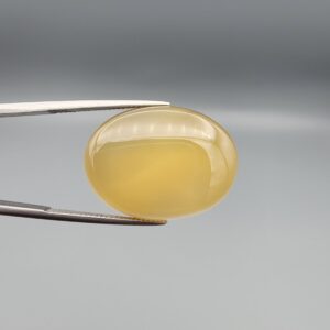 Multi-angle macro photographs of a 31.35-carat natural yellow chalcedony agate (Zard Aqeeq) oval cabochon from Iran held in metal tweezers, showcasing a smooth, domed profile, uniform honey-yellow translucency, and a high-gloss reflective surface.