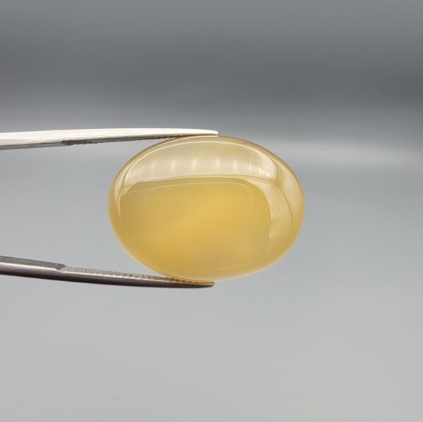 Multi-angle macro photographs of a 31.35-carat natural yellow chalcedony agate (Zard Aqeeq) oval cabochon from Iran held in metal tweezers, showcasing a smooth, domed profile, uniform honey-yellow translucency, and a high-gloss reflective surface.