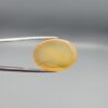 Multi-angle macro photographs of a 31.35-carat natural yellow chalcedony agate (Zard Aqeeq) oval cabochon from Iran held in metal tweezers, showcasing a smooth, domed profile, uniform honey-yellow translucency, and a high-gloss reflective surface.