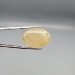 Multi-angle macro photographs of a 29.78-carat natural yellow chalcedony agate (Zard Aqeeq) oval cabochon from Iran held in metal tweezers, showcasing a smooth, domed profile, uniform honey-yellow translucency, and a high-gloss reflective surface.