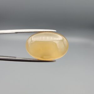 Multi-angle macro photographs of a 17.35-carat natural yellow chalcedony agate (Zard Aqeeq) oval cabochon from Iran held in metal tweezers, showcasing a smooth, domed surface, uniform honey-yellow translucency, and a high-gloss reflective surface.