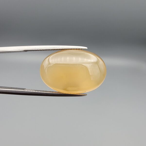 Multi-angle macro photographs of a 17.35-carat natural yellow chalcedony agate (Zard Aqeeq) oval cabochon from Iran held in metal tweezers, showcasing a smooth, domed surface, uniform honey-yellow translucency, and a high-gloss reflective surface.