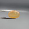 Multi-angle macro photographs of a 17.35-carat natural yellow chalcedony agate (Zard Aqeeq) oval cabochon from Iran held in metal tweezers, showcasing a smooth, domed surface, uniform honey-yellow translucency, and a high-gloss reflective surface.