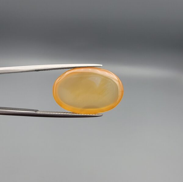 Multi-angle macro photographs of a 17.35-carat natural yellow chalcedony agate (Zard Aqeeq) oval cabochon from Iran held in metal tweezers, showcasing a smooth, domed surface, uniform honey-yellow translucency, and a high-gloss reflective surface.